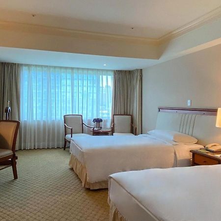 Evergreen Laurel Hotel - Taichung Exterior foto The photo shows a hotel room featuring two single beds positioned near each other. There's a light-colored carpet on the floor and a large window with sheer curtains that allows natural light to fill the space. In the room, there are two chairs place
