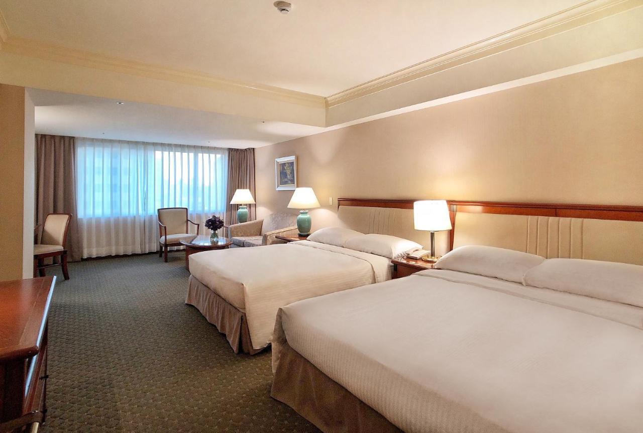 Evergreen Laurel Hotel - Taichung Exterior foto The photo shows a hotel room featuring two queen-sized beds with white linens. The room is well-lit and has a warm, neutral color palette. There are bedside lamps on each side of the beds and a small table. To the side, there's a comfortable armchair