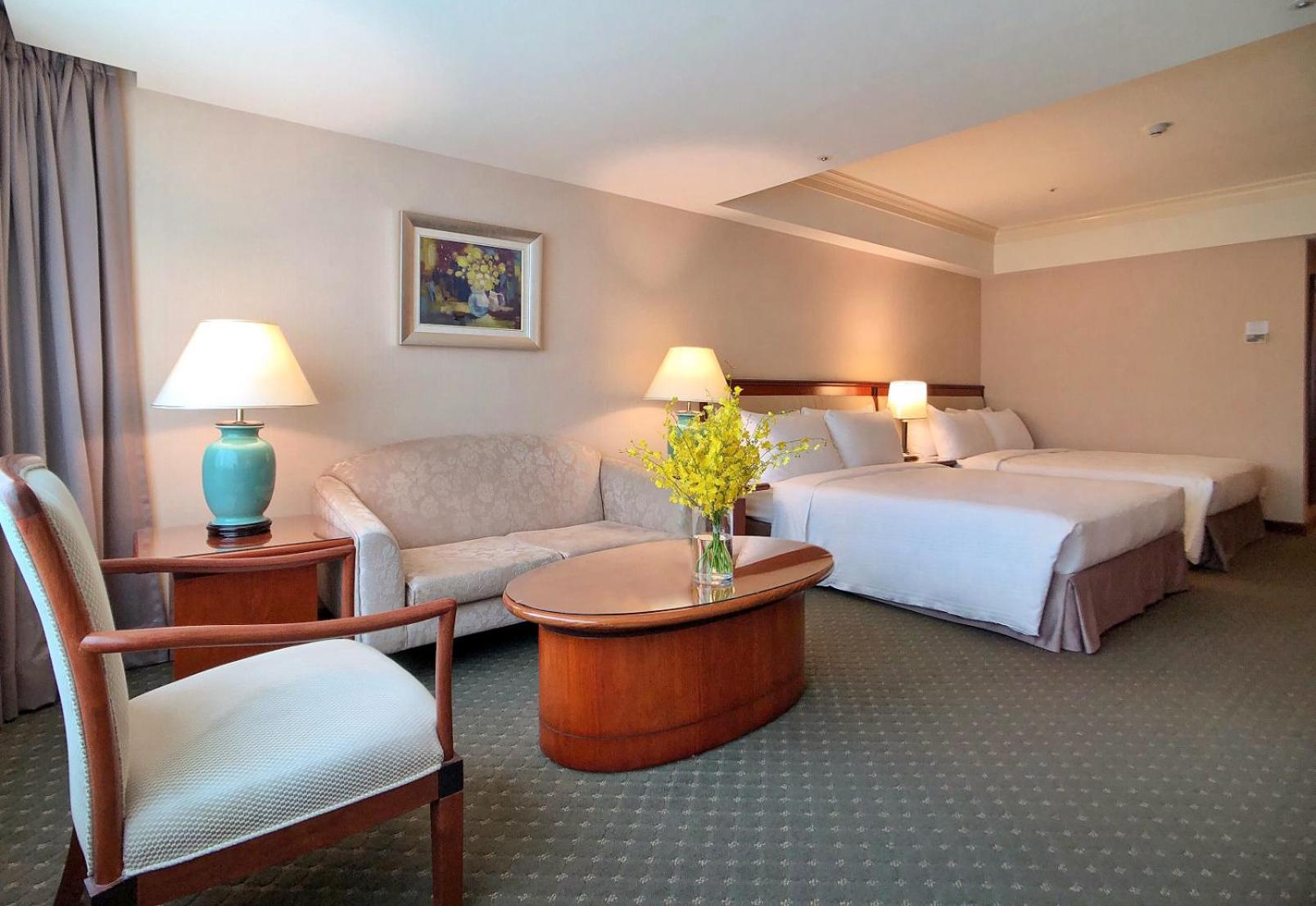 Evergreen Laurel Hotel - Taichung Exterior foto The photo shows a hotel room featuring two beds, a small seating area, and a coffee table. The walls are painted in soft, neutral colors, and there is a framed piece of artwork hanging on the wall. A potted plant with yellow flowers is placed on the 