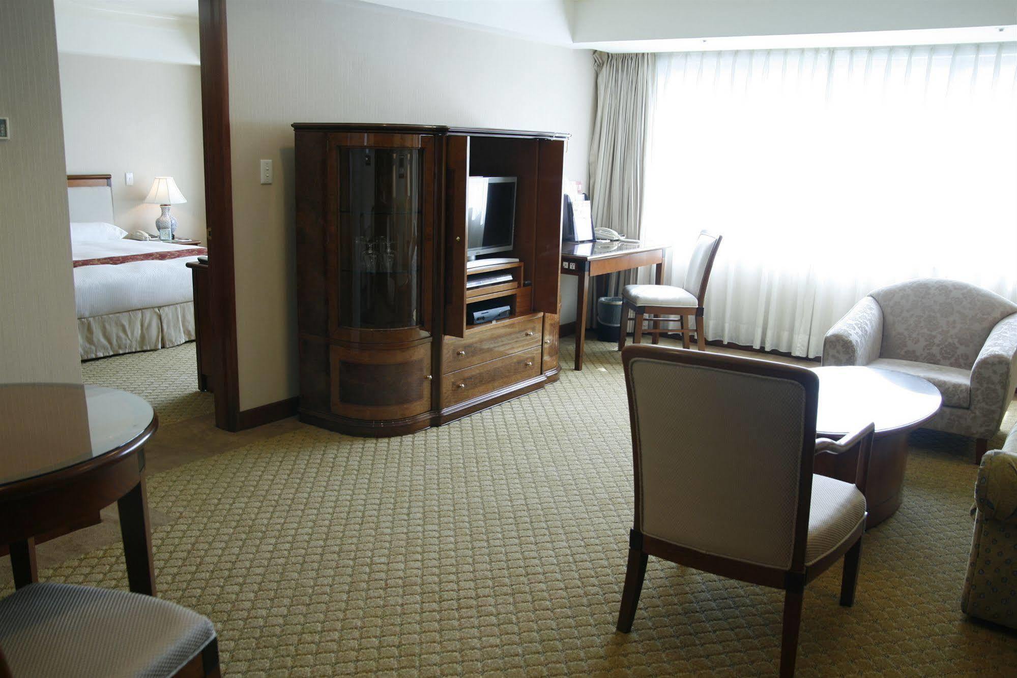 Evergreen Laurel Hotel - Taichung Exterior foto The photo shows an interior of a hotel room suite. The space includes a living area with several pieces of furniture. There is a coffee table and chairs, creating a comfortable seating area. A wooden cabinet with a TV inside is situated against one w