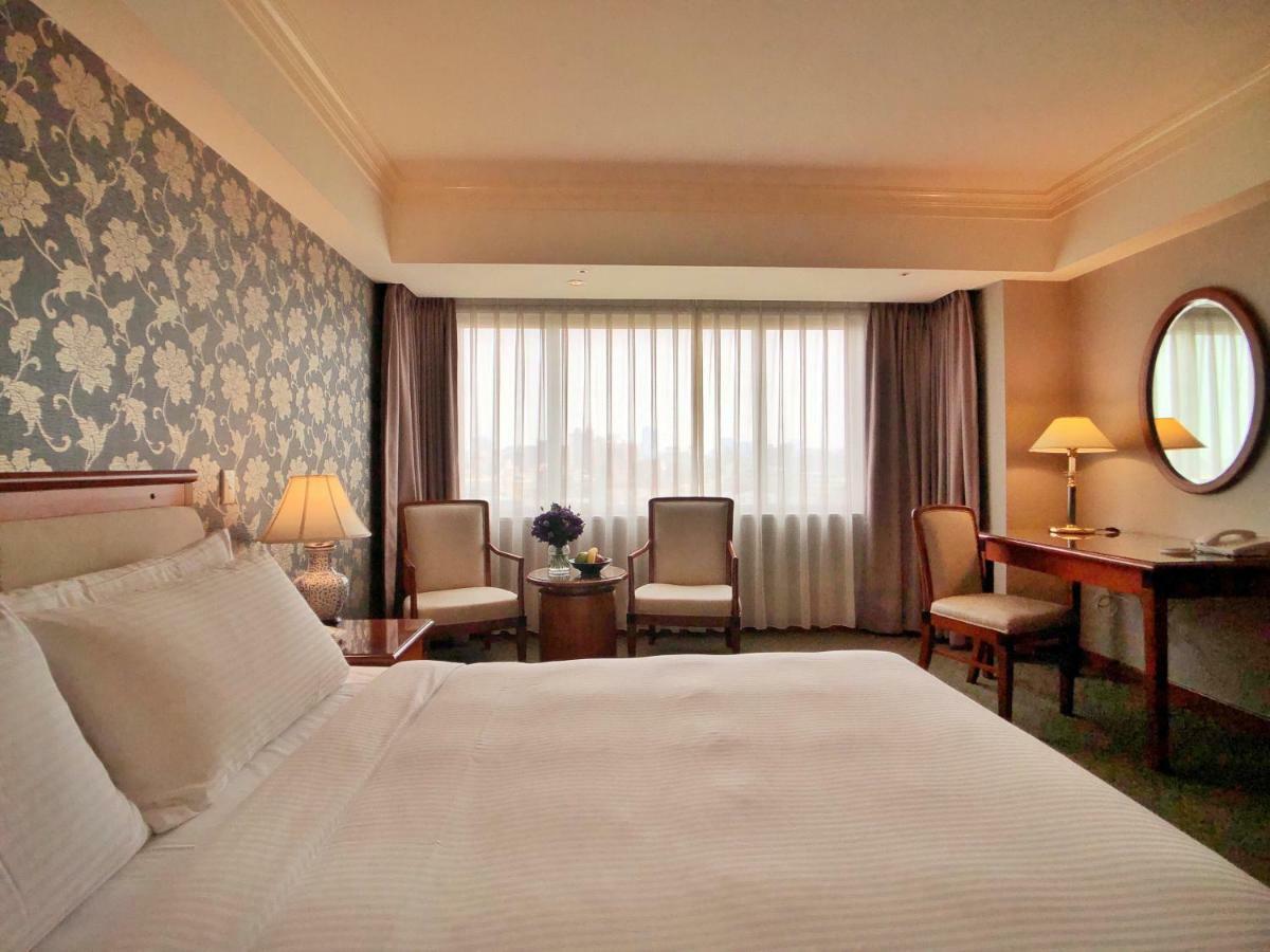 Evergreen Laurel Hotel - Taichung Exterior foto The photo shows a hotel room with a comfortable and inviting design. There is a large bed with crisp white bedding on the left side of the image. To the right, there are two elegant chairs with a small round table between them, adorned with a bouquet