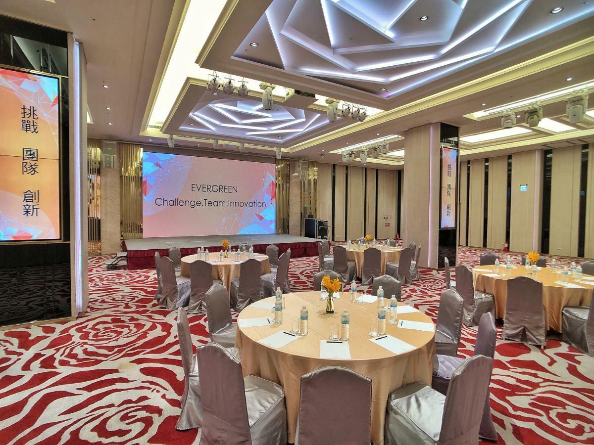 Evergreen Laurel Hotel - Taichung Exterior foto The photo shows a conference or event space set up for a gathering. The room features several round tables with light-colored tablecloths and chairs, each with decoration, possibly for dining or discussion. A large screen displays the text "EVERGREEN